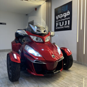 A 2015 Can-Am Spyder RT touring trike in glossy white with full touring fairings, large windscreen, comfortable passenger backrest, side panniers, and rear top case, parked outdoors with its three-wheel stance clearly visible.